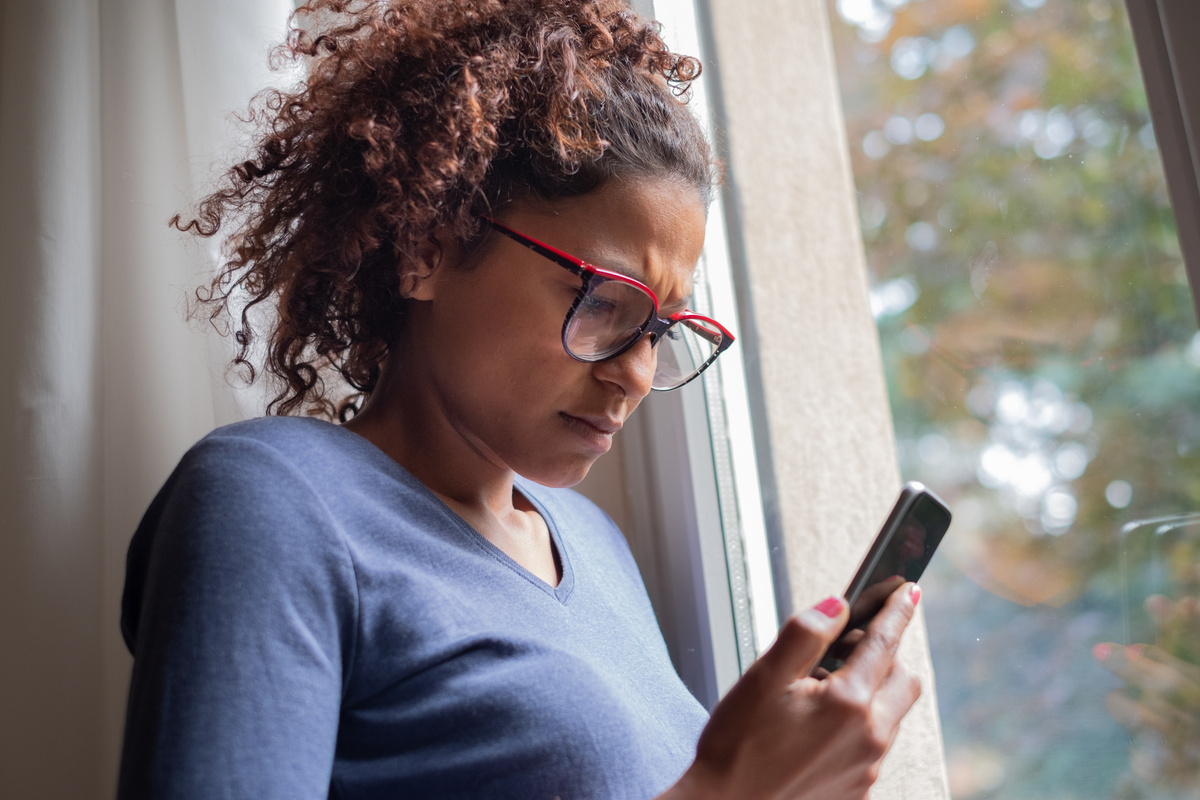 Sad black woman near window reading phone message